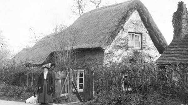 Jane Cook and dog in front of thatched cottage